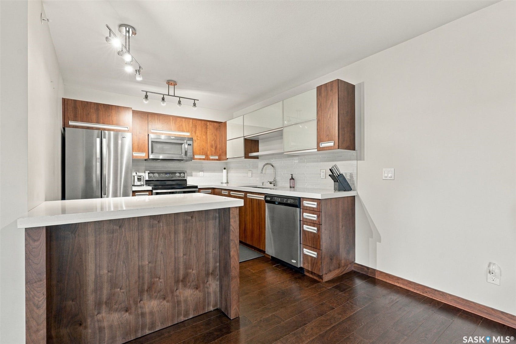 Wood-finish flooring throughout, stainless steel appliances, wood-finish cabinetry, white countertops, and subway tile backsplash
