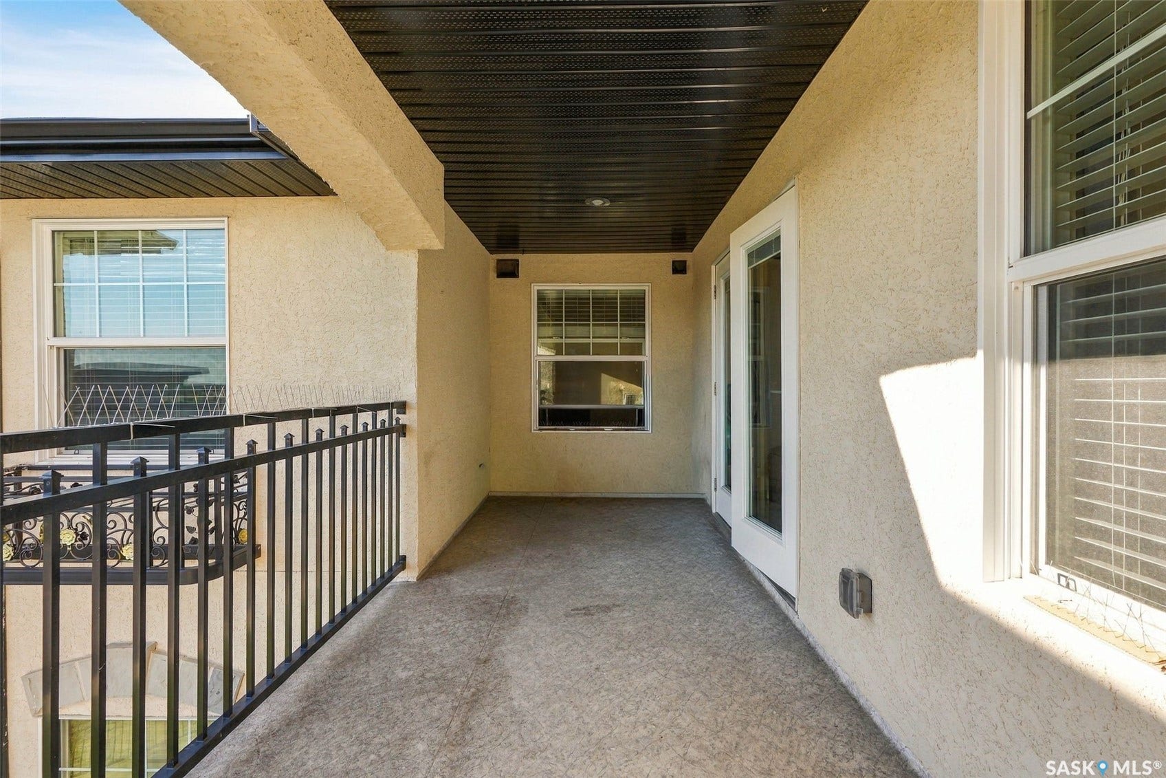Balcony featuring stucco exterior, a black metal railing, and a textured concrete surface