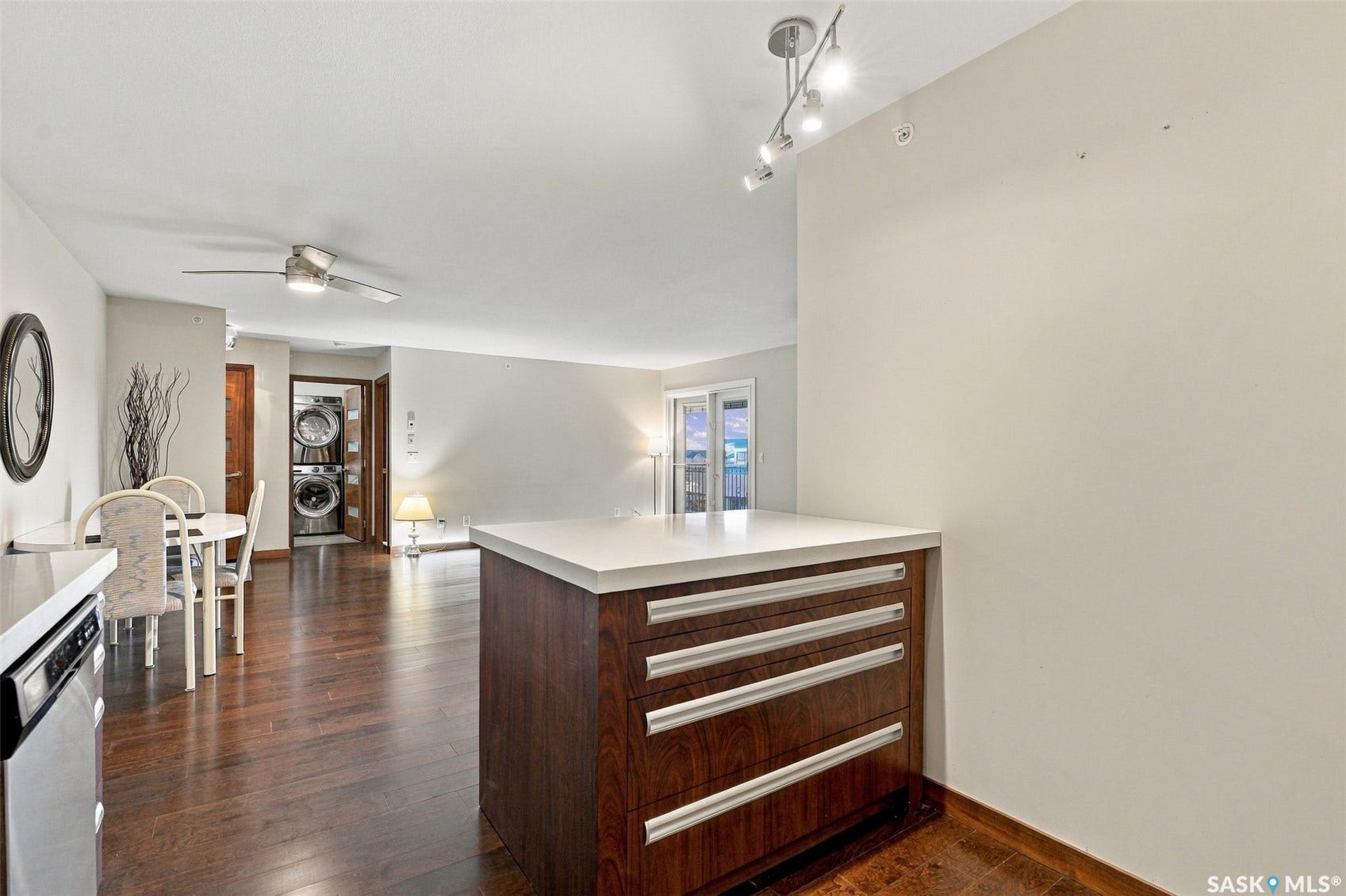 Wood-finish flooring throughout, track lighting, ceiling fan, built-in kitchen island with drawer storage, and stacked laundry appliances