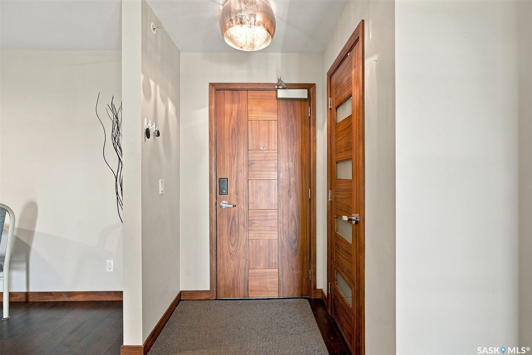 Wood-finish flooring with coordinating wood trim, modern wood panel entry door, and recessed lighting fixture