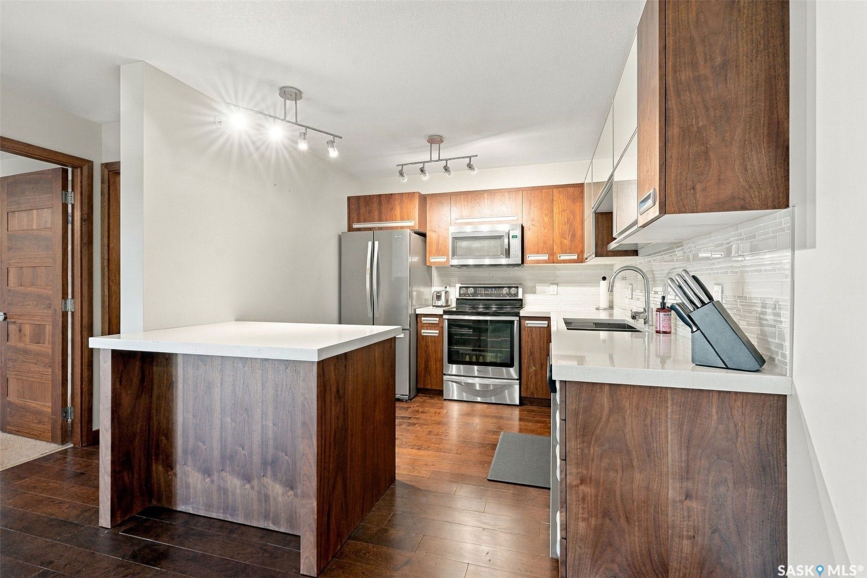 Kitchen featuring wood-finish flooring, stainless steel appliances, white countertops, a mosaic tile backsplash, and track lighting fixtures