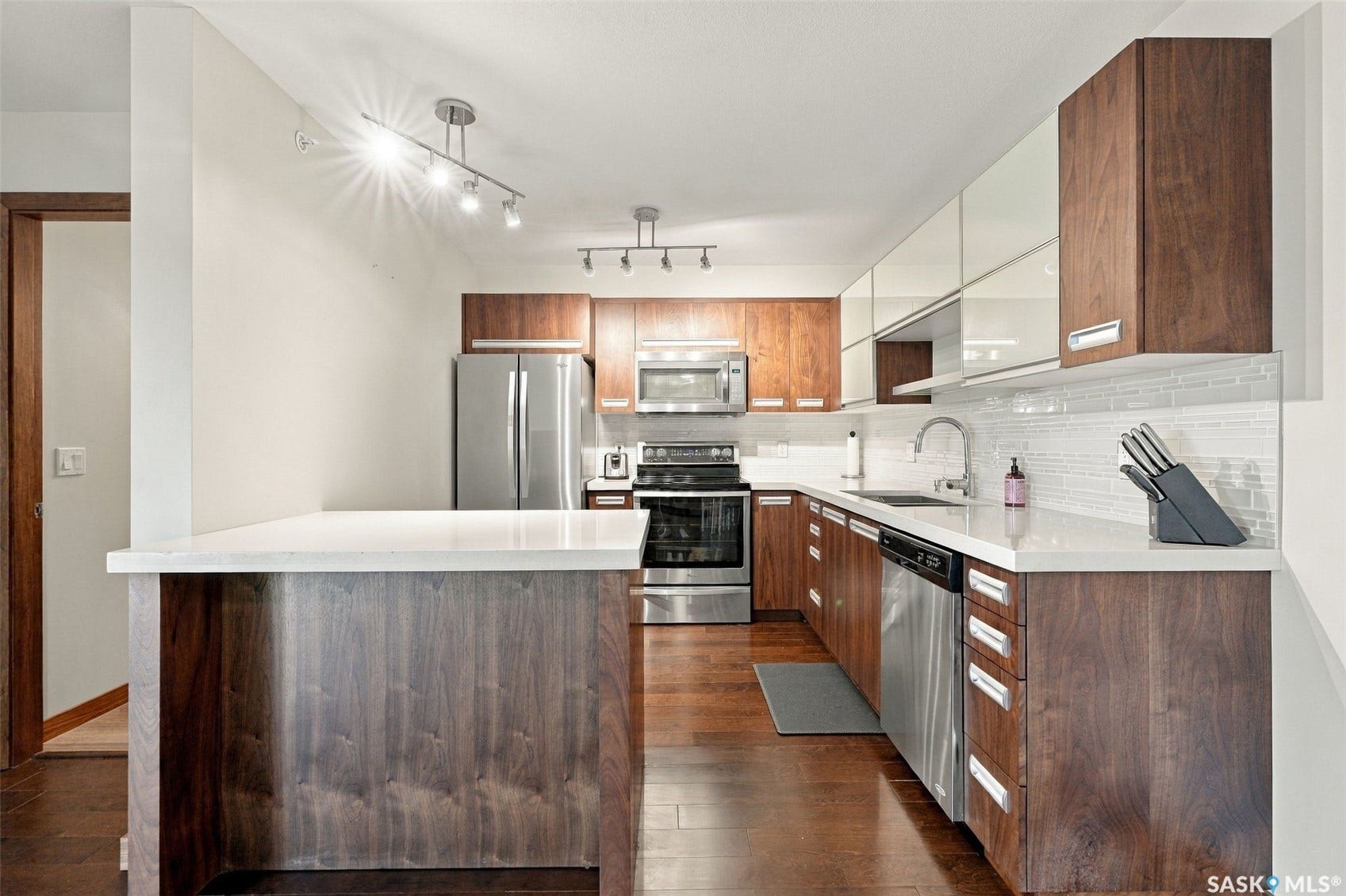 Kitchen featuring wood-finish cabinetry, stainless steel appliances, a white tile backsplash, and a breakfast bar with a solid surface countertop