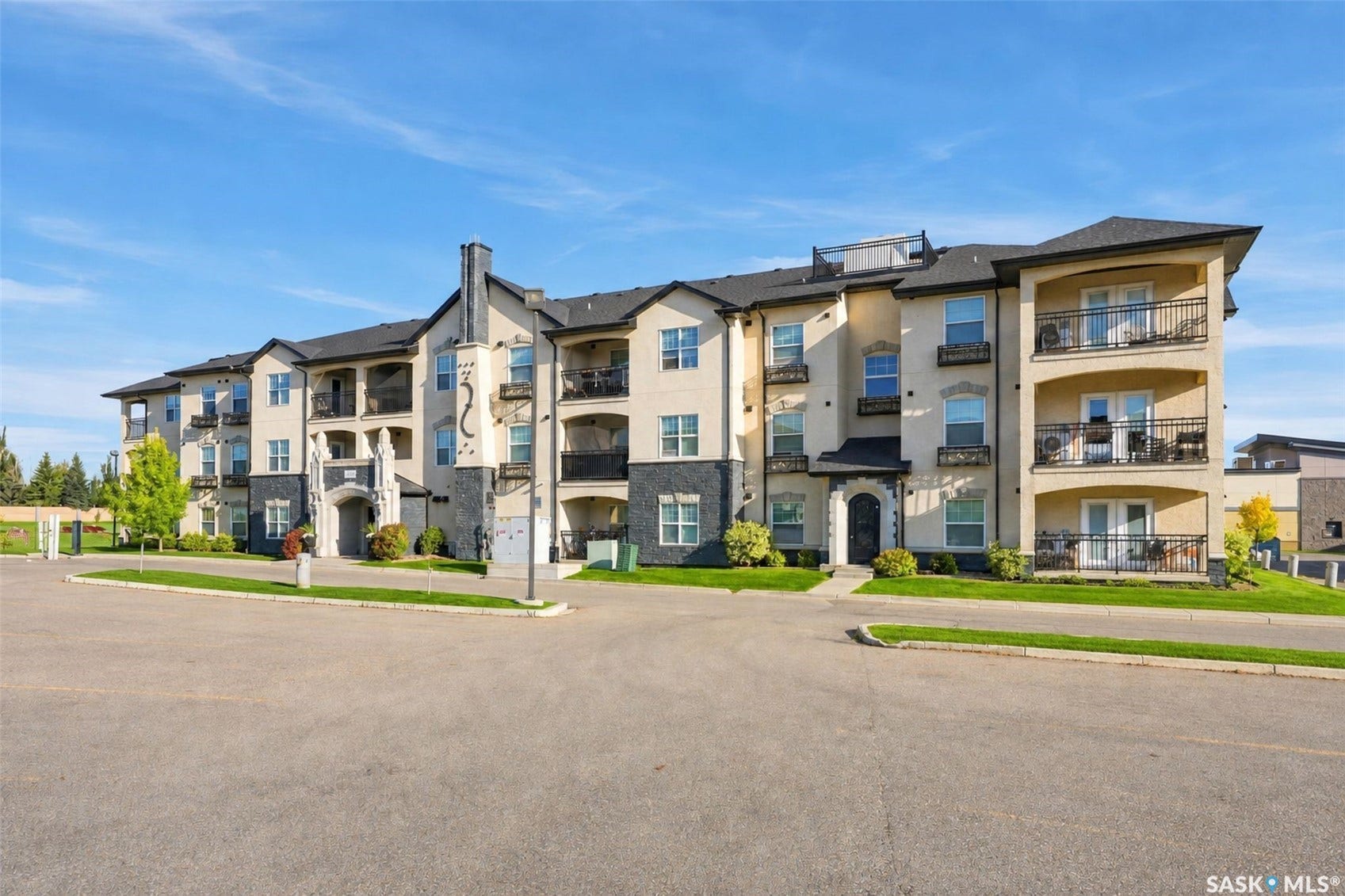 Four-story multi-unit building featuring stucco and stone veneer exterior, multiple balconies with wrought iron railings, and a dark shingled roof