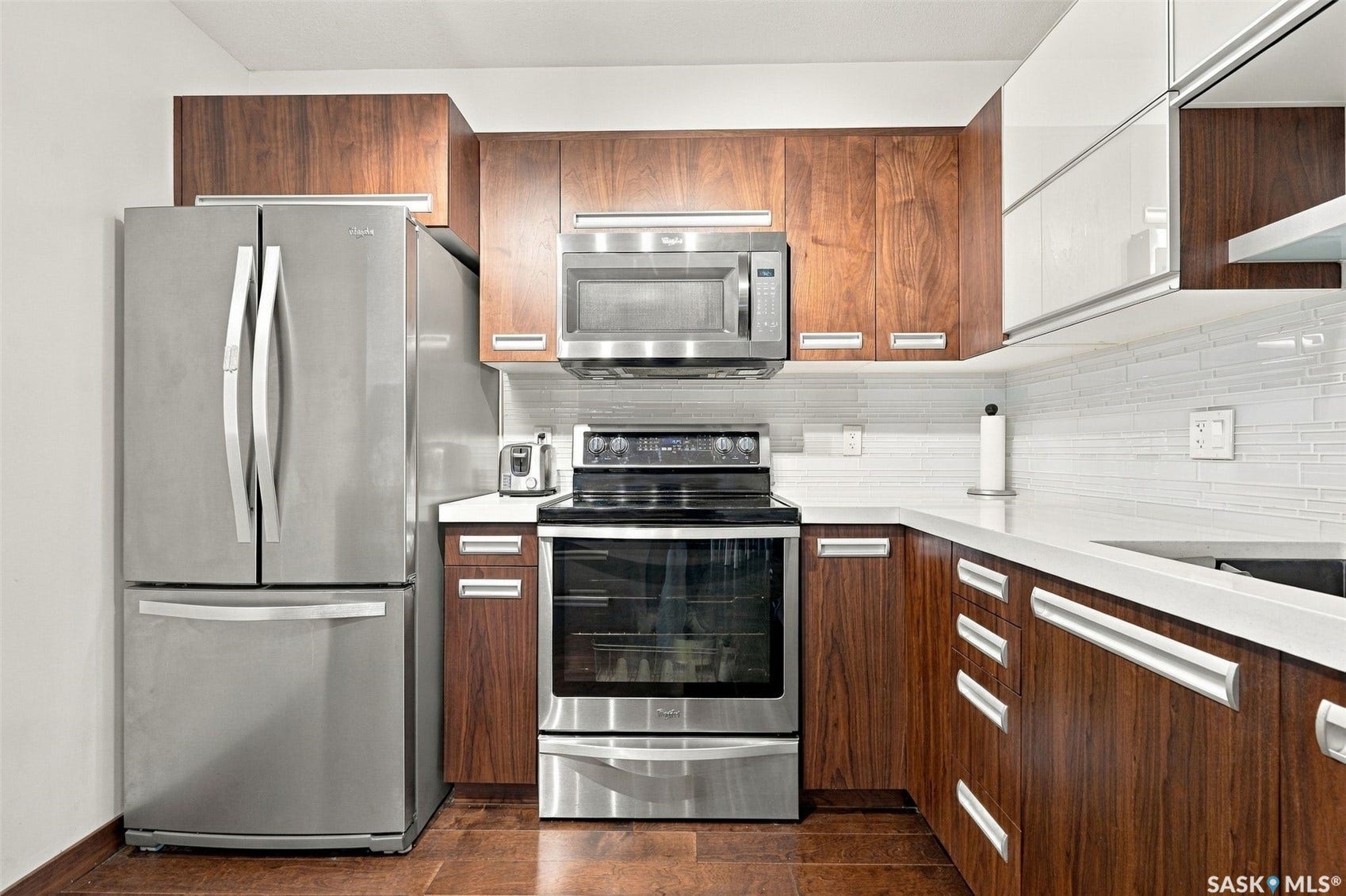 Stainless steel appliances, white countertops, mosaic tile backsplash, wood-finish cabinetry, and wood-finish flooring