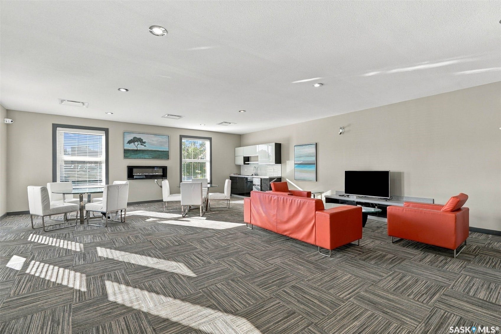 Recessed lighting illuminates an open space featuring patterned carpet, multiple windows, and a built-in fireplace
