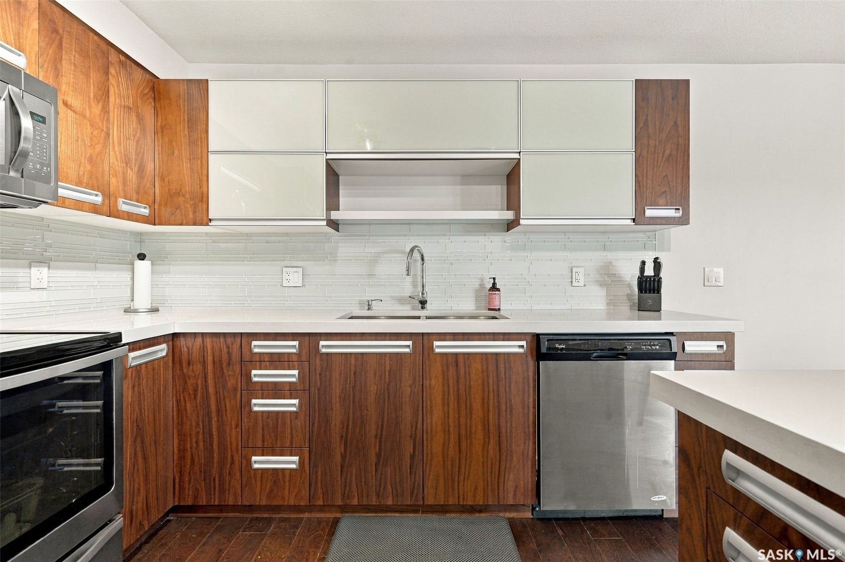 Modern kitchen featuring wood-finish cabinetry, frosted glass upper cabinets, stainless steel appliances, white subway tile backsplash, and light-toned countertops