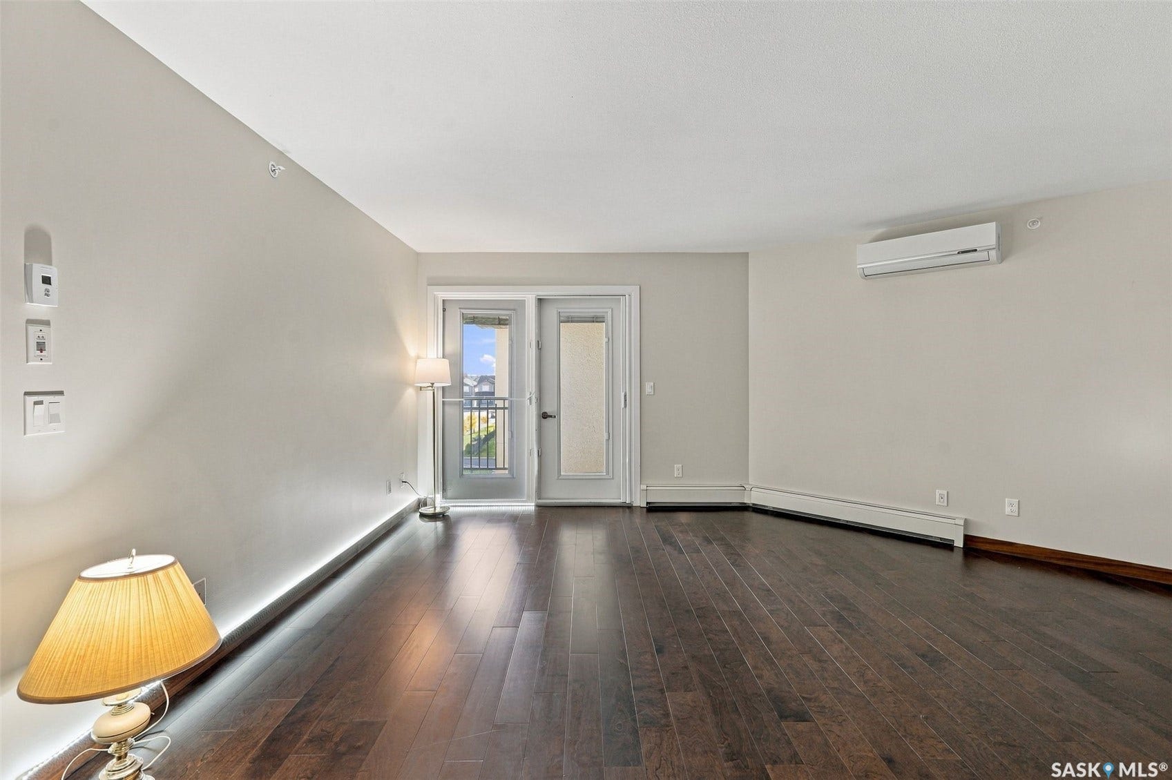 Dark wood-finish flooring with a split-system air conditioning unit, baseboard heating, and French doors leading to a balcony