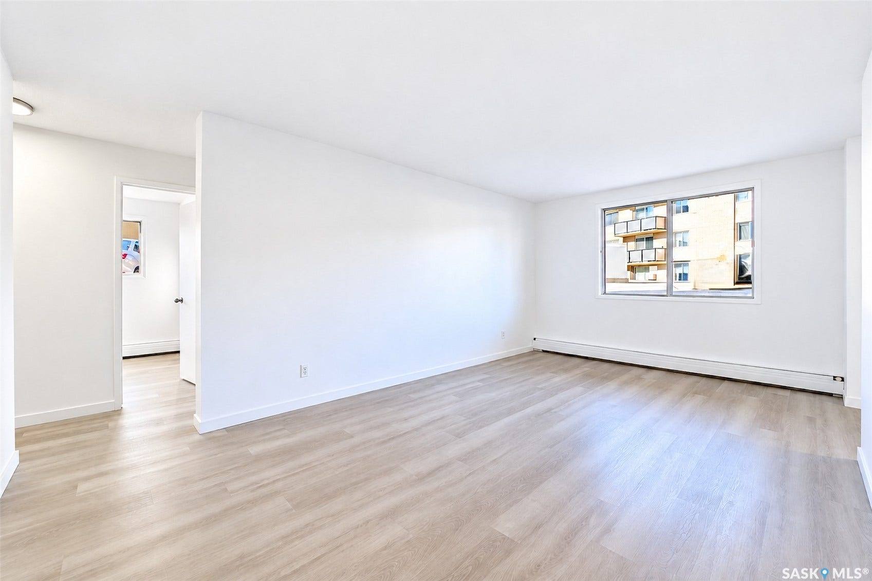 Wood-finish flooring throughout, bright white walls, and a large window with exterior building visibility