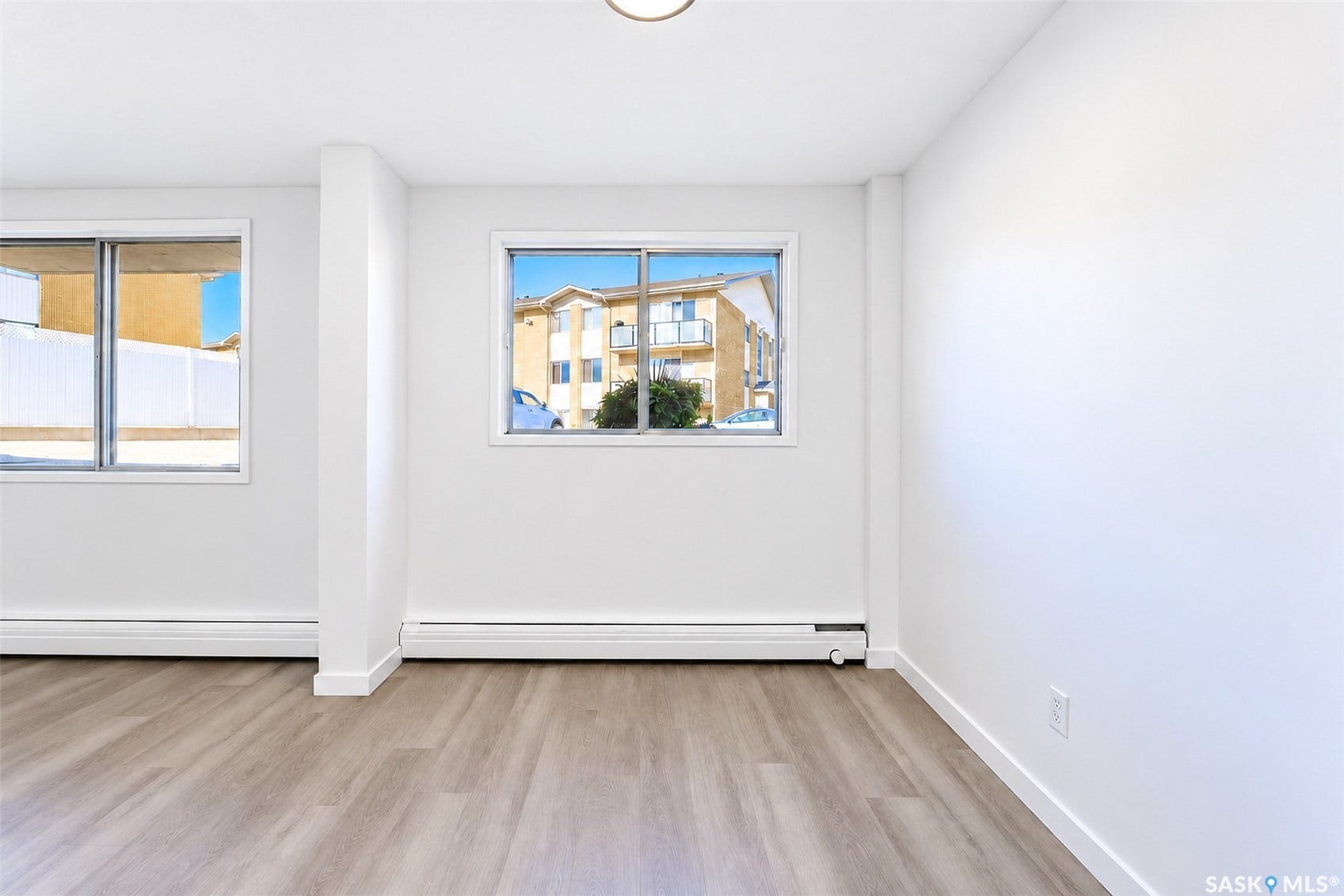 Bright interior space featuring wood-finish flooring, white walls, and dual windows