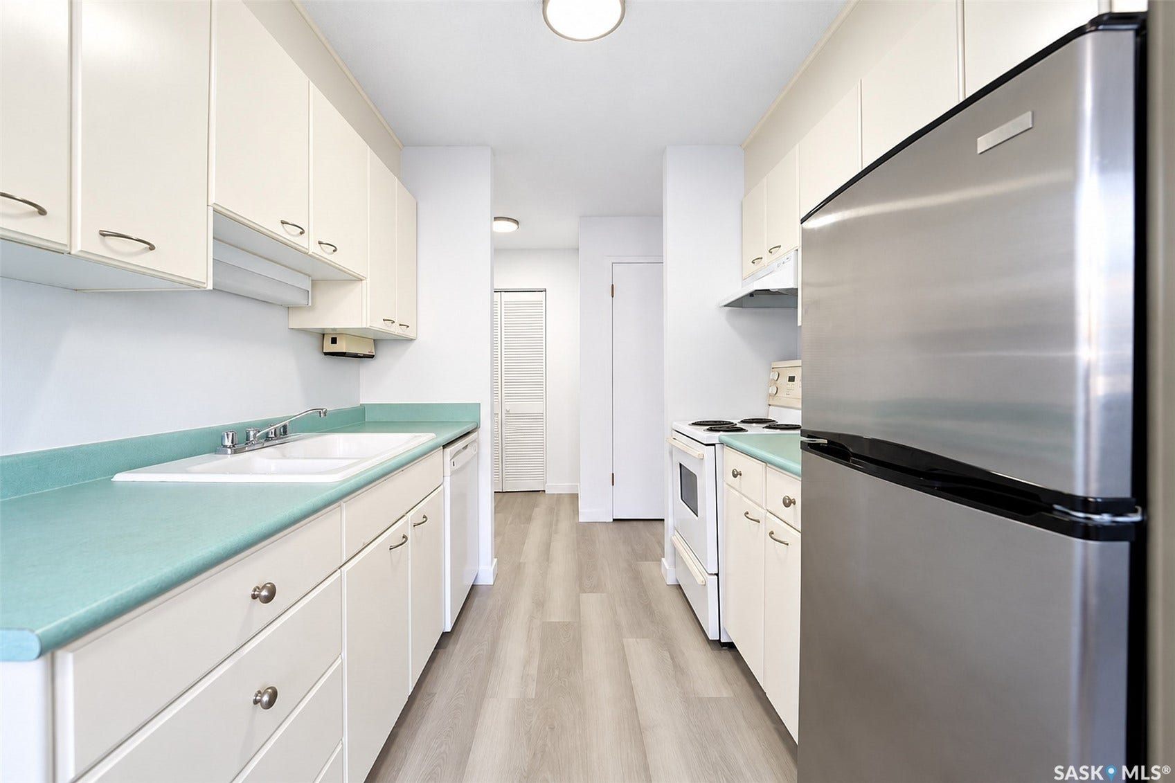 Galley kitchen featuring ample white cabinetry, a double basin sink, light wood-finish flooring, and a stainless steel refrigerator