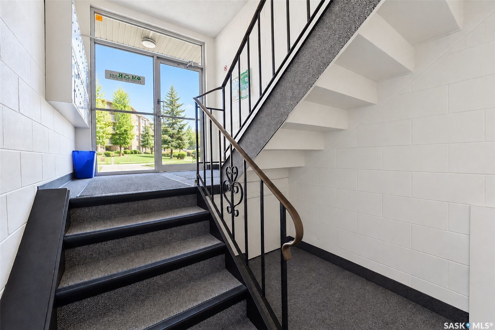 Carpeted staircase with wrought iron railing, white block walls, and a glass-paneled entry door