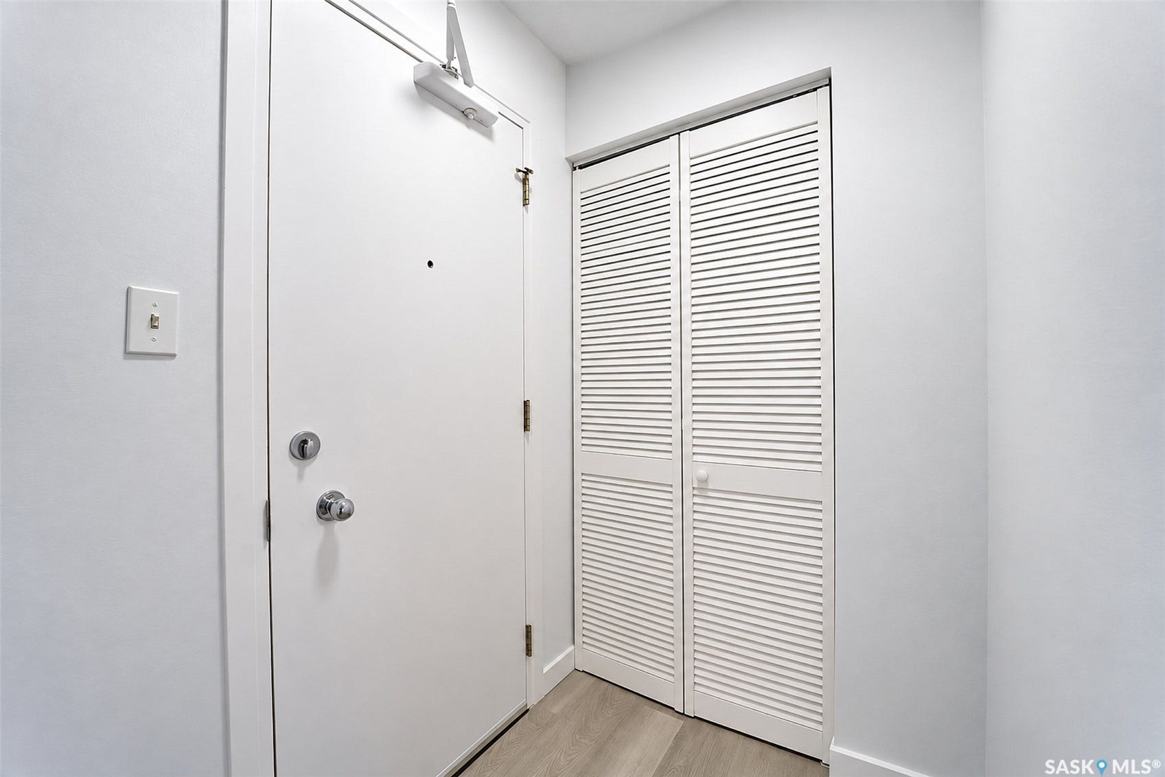 White interior door with chrome hardware, bi-fold louvered closet doors, and light wood-finish flooring