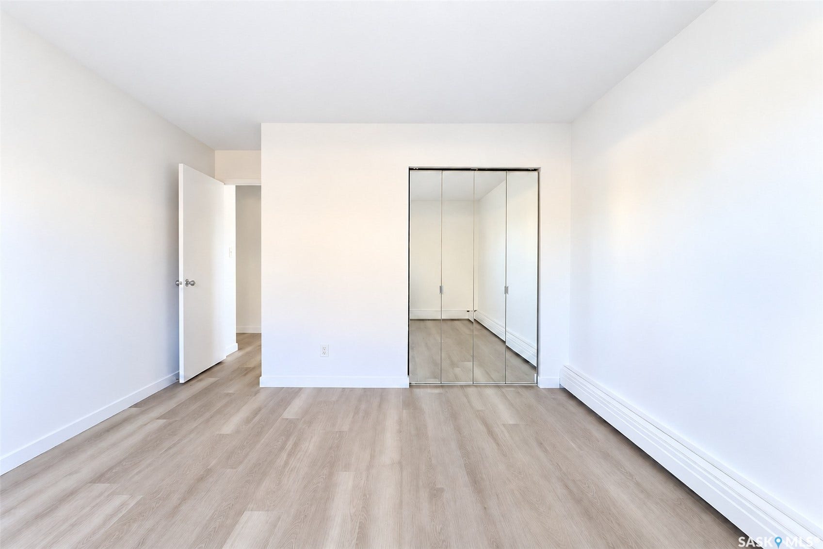 White painted walls, wood-finish flooring, mirrored closet doors, and white baseboard trim
