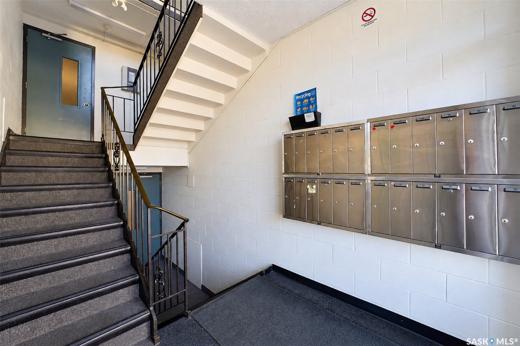 Building entryway featuring a staircase with metal railings, white block wall, and integrated mailboxes