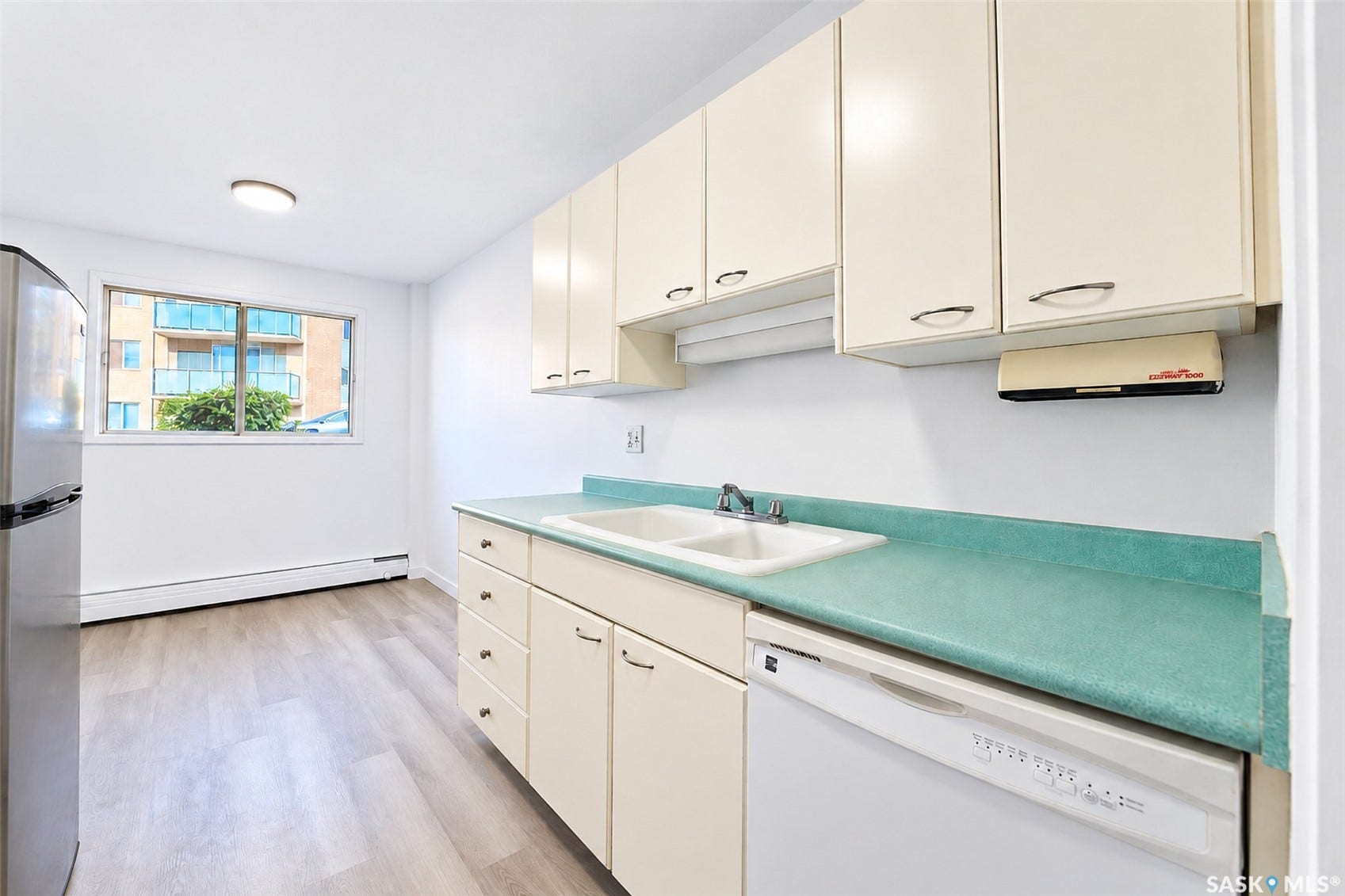 Kitchen featuring light-toned cabinetry, light-toned wood-finish flooring, a double basin sink, and a dishwasher