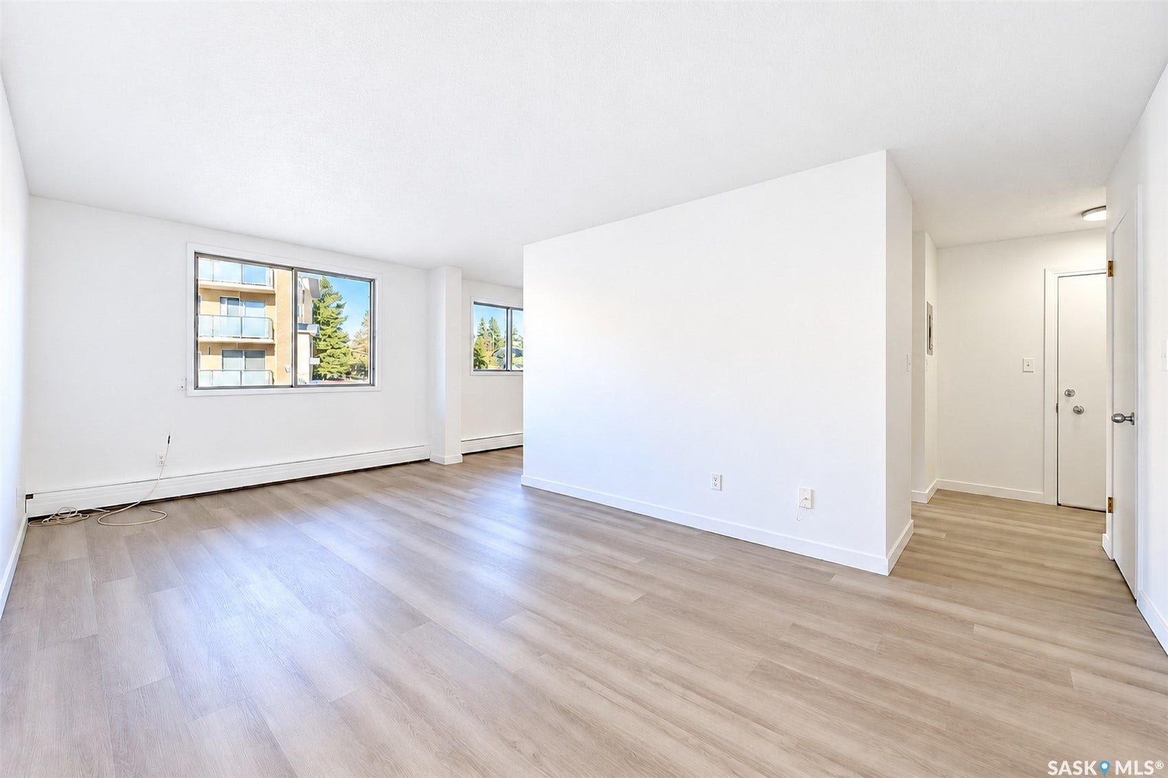 Spacious room with wood-finish flooring, two large windows, and a doorway with a flush-mounted ceiling light