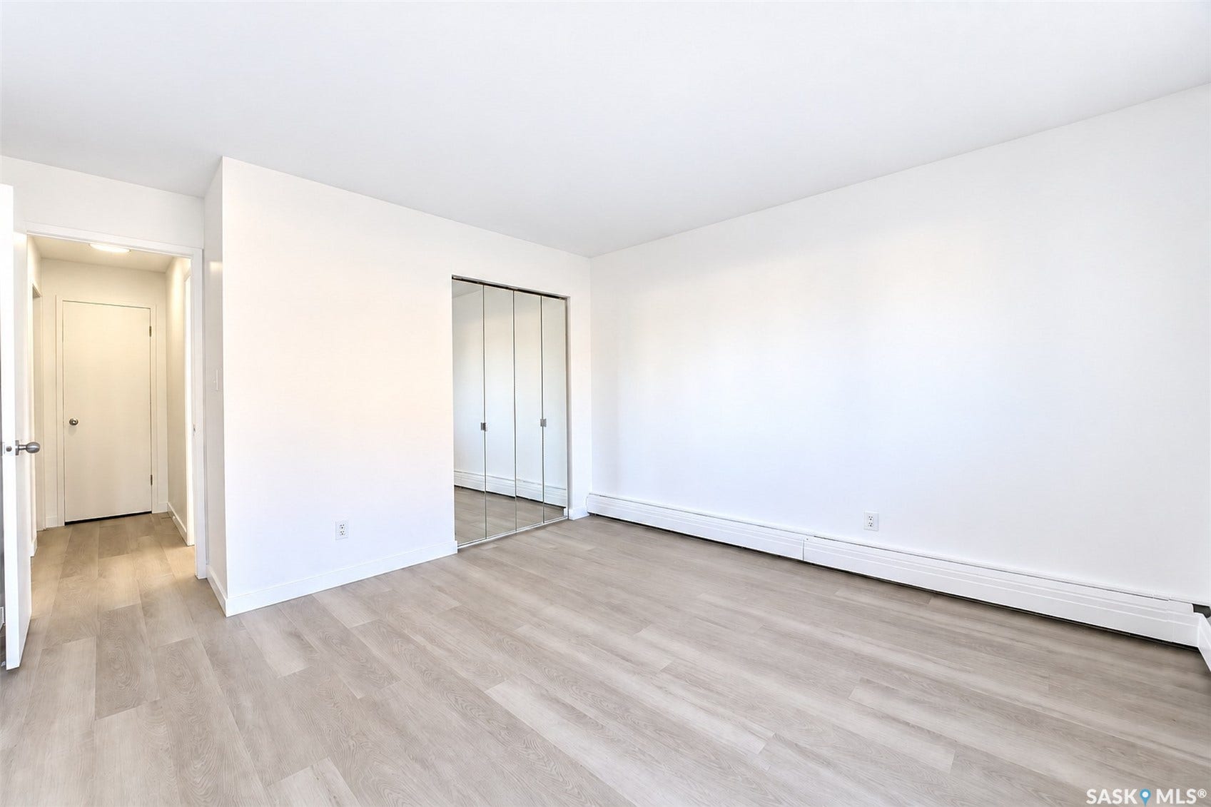 Light-toned wood-finish flooring, white walls, and mirrored closet doors