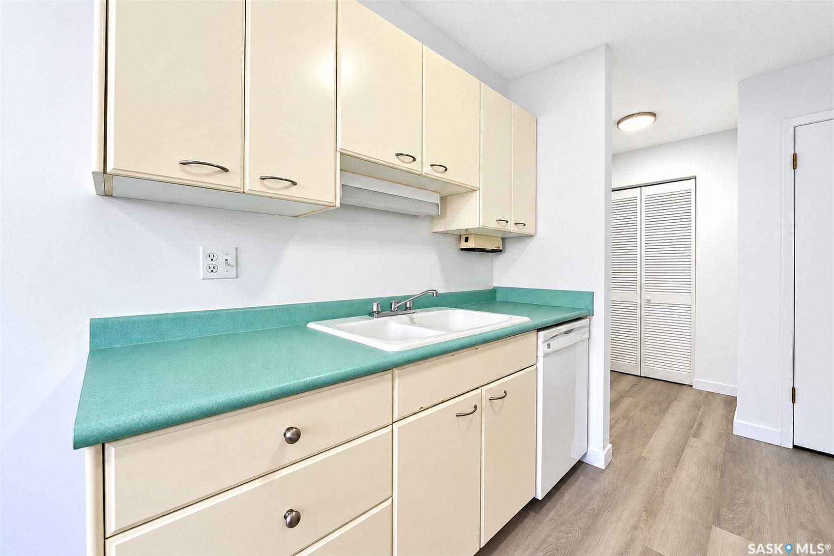 Cream-toned cabinetry with metal hardware, double basin sink, integrated dishwasher, teal countertop, and wood-finish flooring