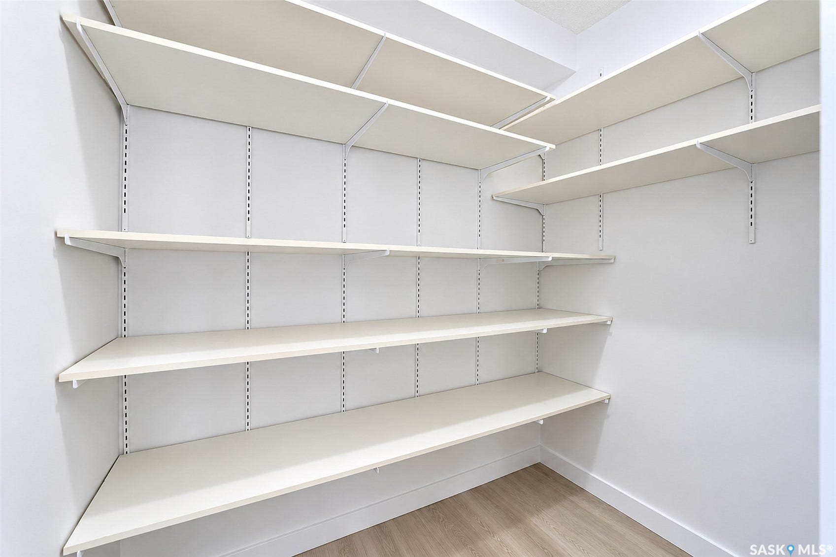 Customizable shelving system with multiple shelves, light wood-finish flooring, and white walls
