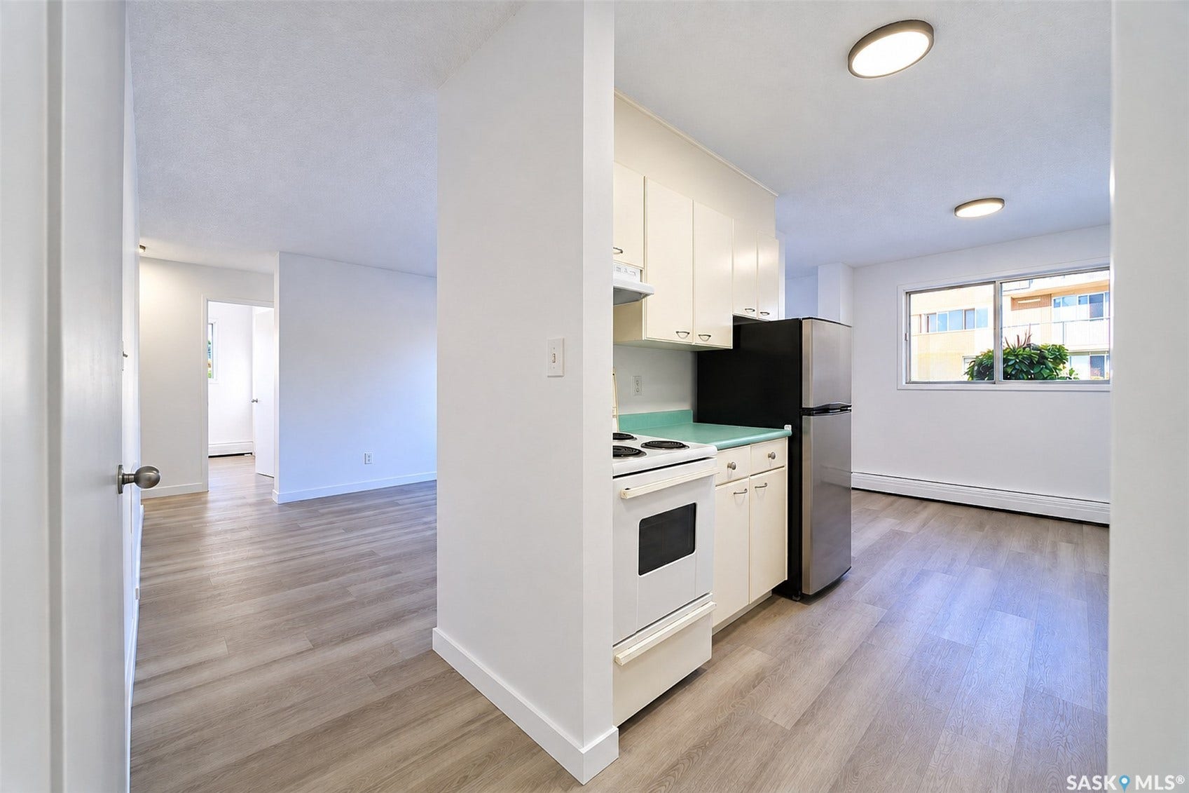 Wood-finish flooring throughout, white cabinetry, stainless steel refrigerator, white range, and a large window