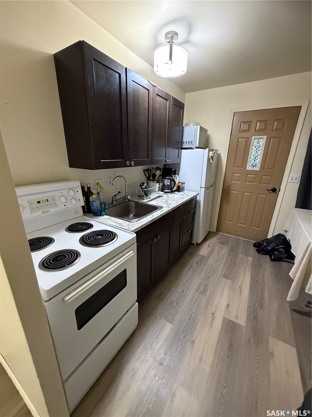 301 2nd Street, #1-10, Kennedy SK S0G 2R0 Kitchen featuring wood-finish flooring, dark wood cabinetry, a stainless steel sink, a white freestanding range, and a ceiling-mounted light fixture