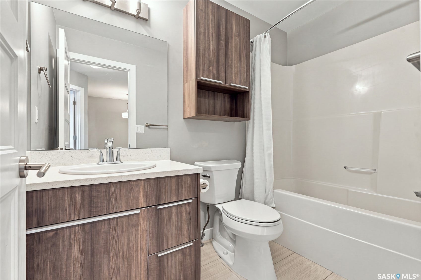 Bathroom featuring a wood-finish vanity with a light-colored countertop, an undermount sink, a wall-mounted mirror, and a built-in shower/tub combination