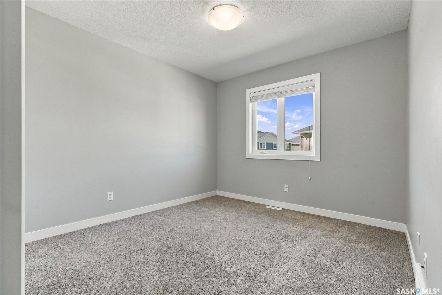 Bright, versatile bedroom featuring neutral gray walls, soft-close electrical outlets, and abundant natural light from a large double-hung window