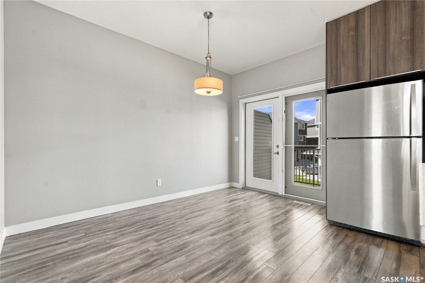 Wood-finish flooring, contemporary pendant lighting, light gray wall tones, stainless steel refrigerator, and wood-grain cabinetry