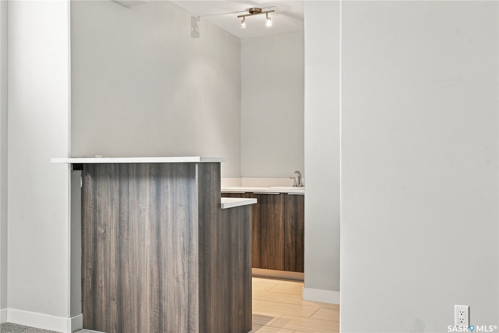 Built-in bar with wood-finish cabinetry, light-toned countertop, and undermount sink with a chrome faucet
