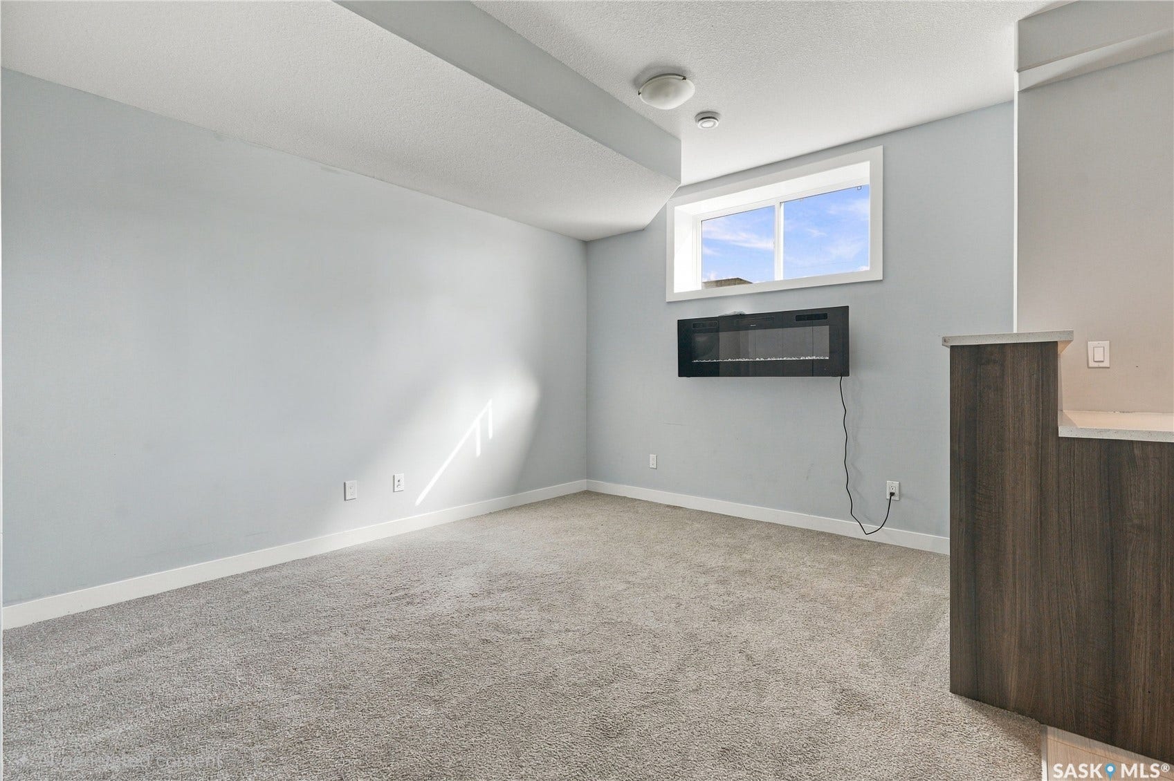 Carpeted flooring, recessed lighting, and a wall-mounted fireplace enhance the space