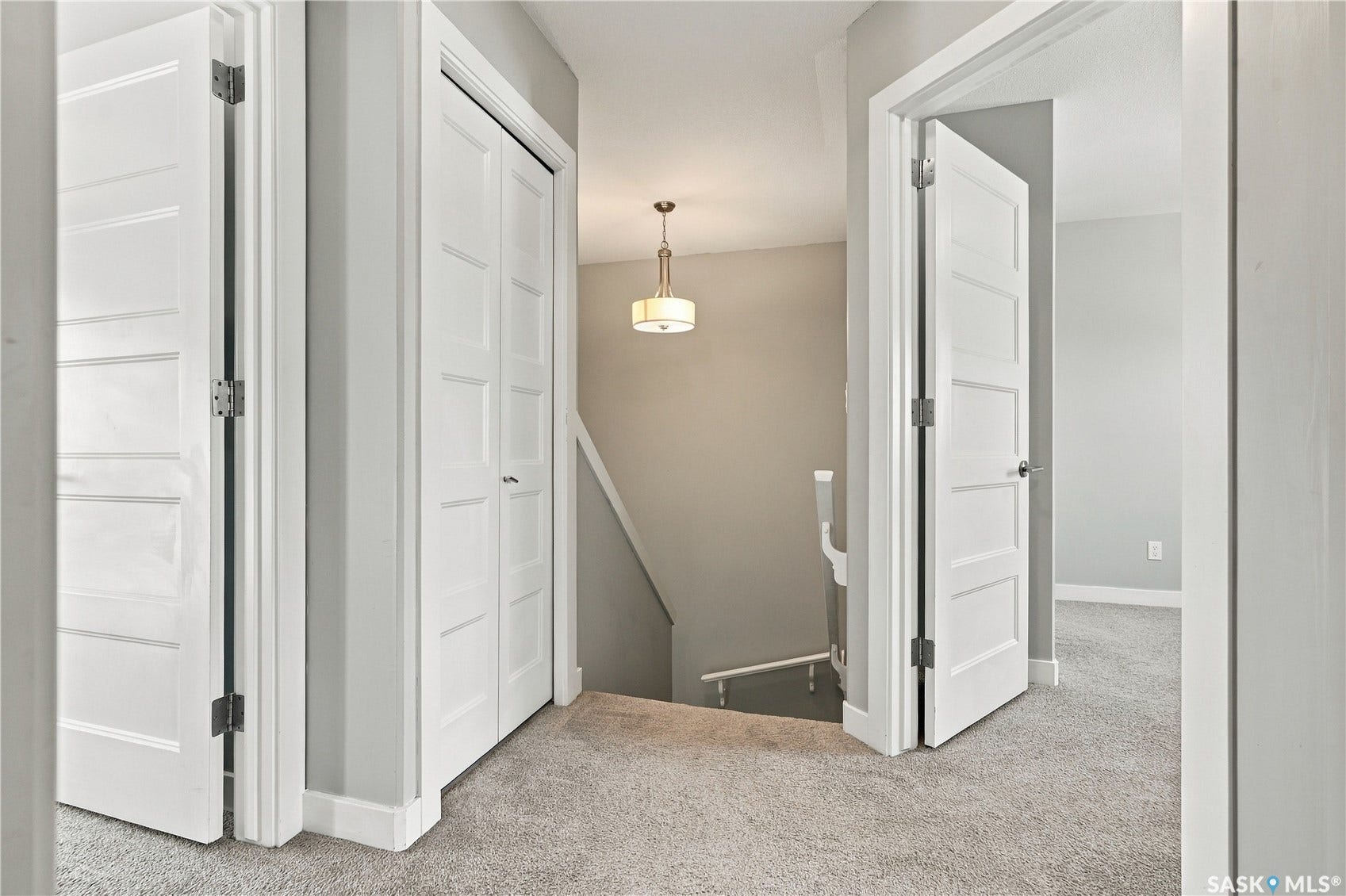 Carpeted hallway featuring white paneled doors, a built-in closet with bifold doors, and a staircase with a white handrail