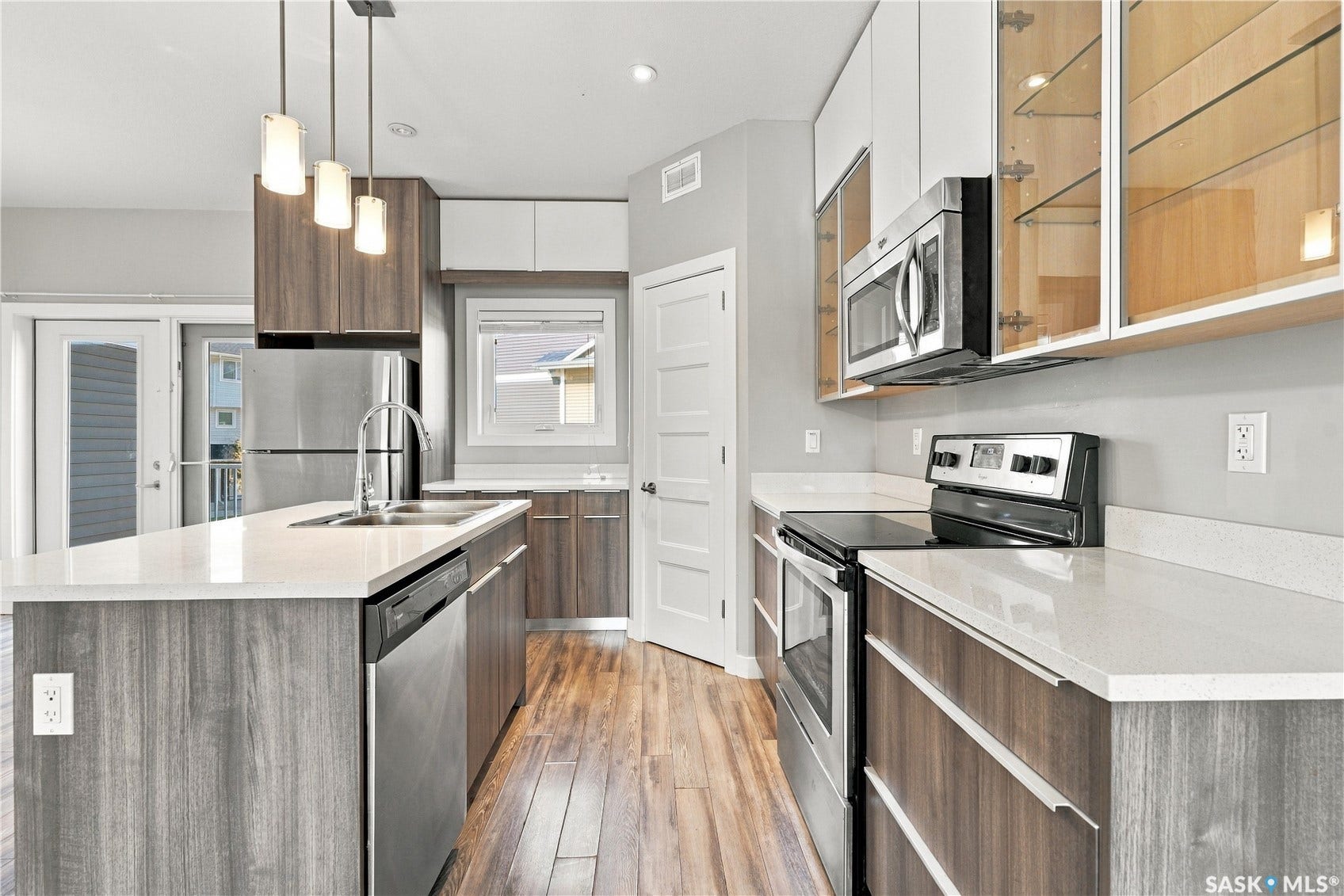Kitchen featuring wood-finish flooring, two-tone cabinetry, stainless steel appliances, a center island with sink, and light-toned countertops