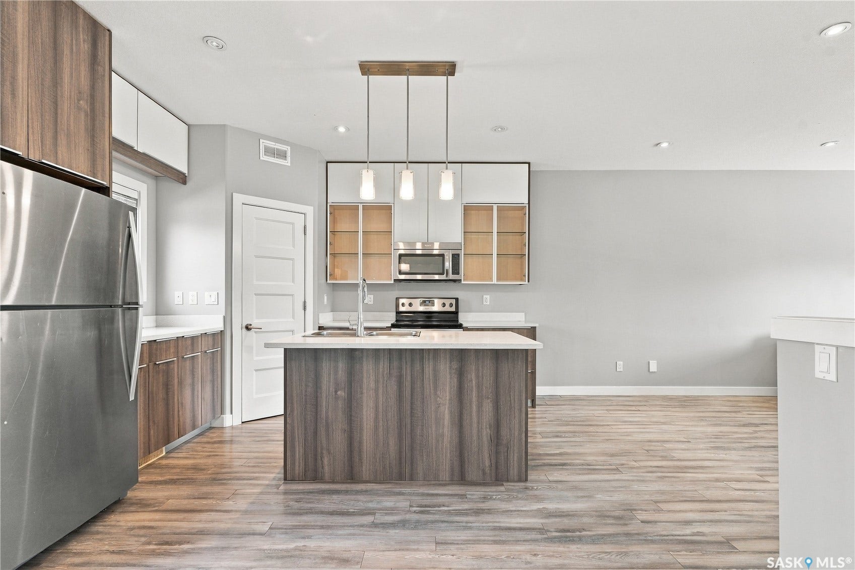 Kitchen featuring stainless steel appliances, wood-finish flooring, an island with a sink, and pendant lighting