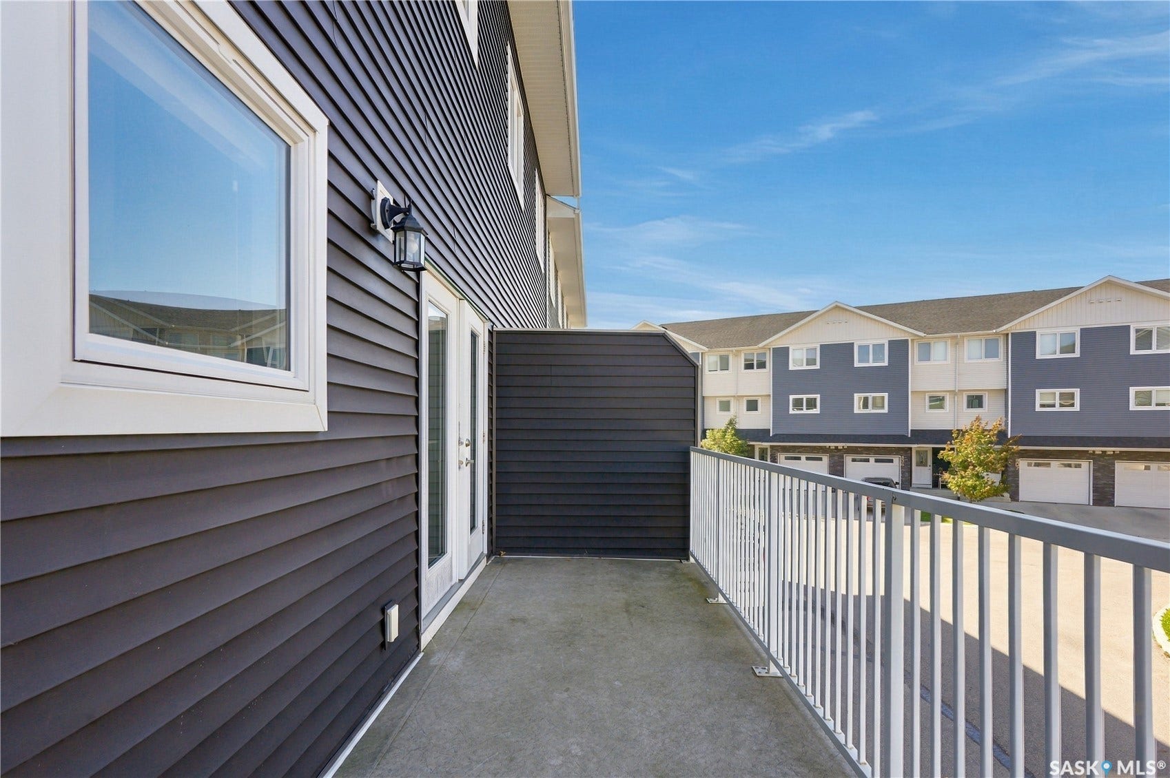 Spacious composite deck featuring concrete flooring, white aluminum railings, and black horizontal siding with large picture window framing neighborhood vistas