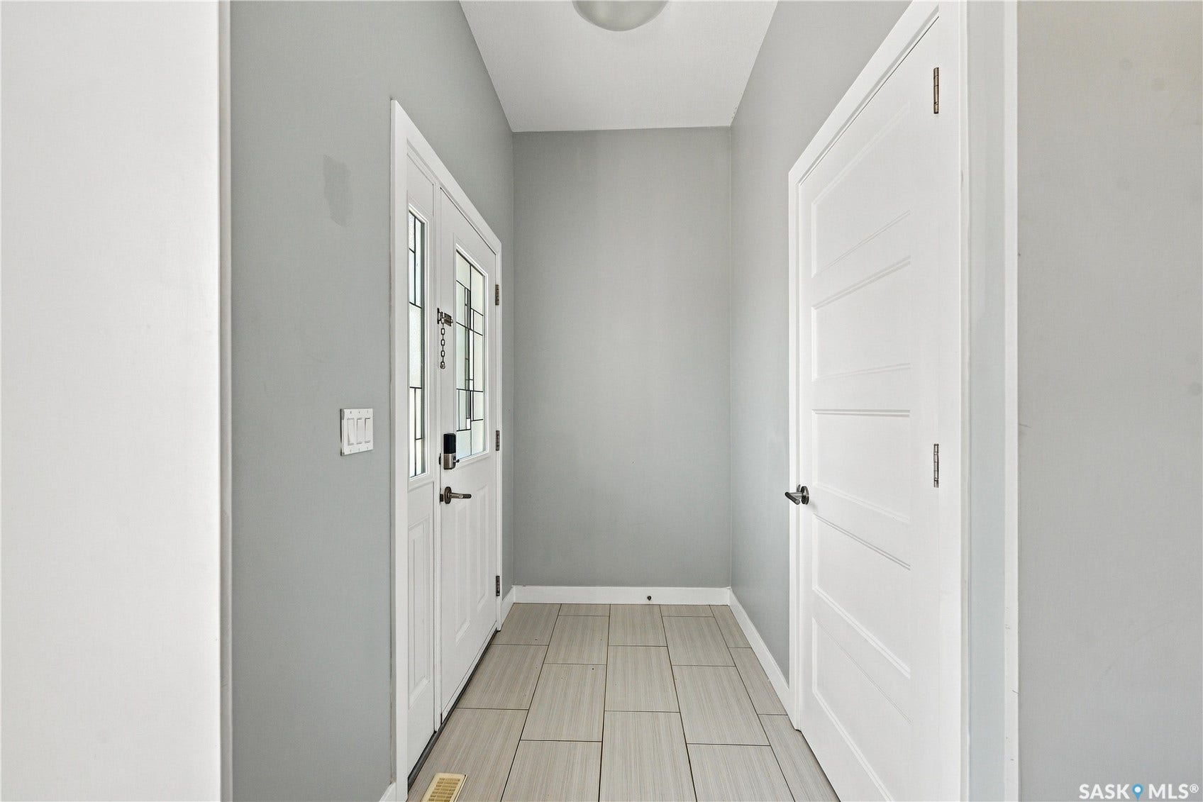 Entryway featuring a white paneled door with decorative glass inserts, light grey wall paint, and light-toned rectangular tile flooring