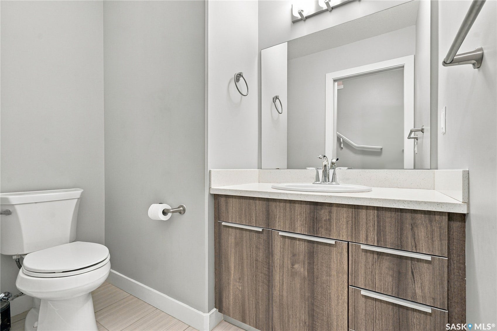 Wood-finish vanity with an integrated sink and light-toned countertop, complemented by a large wall-mounted mirror
