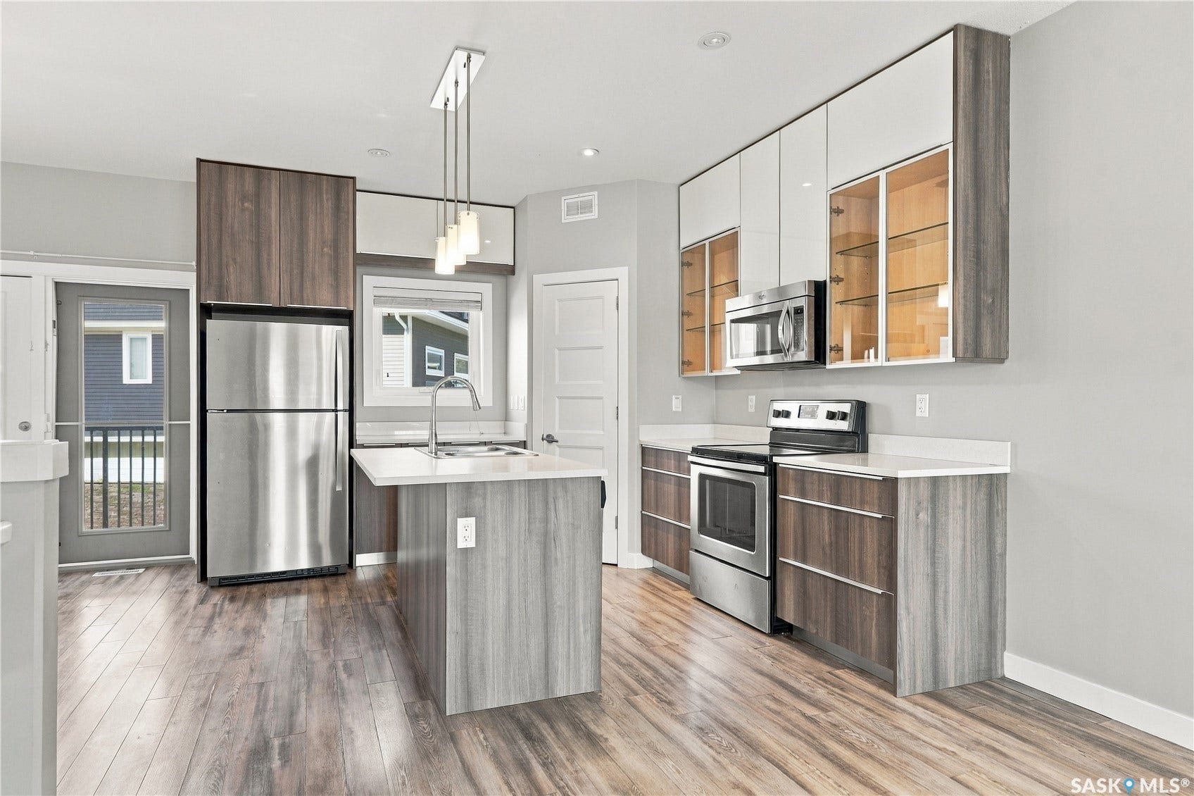 Kitchen featuring stainless steel appliances, wood-finish flooring, two-tone cabinetry, a central island with a sink, and a built-in microwave