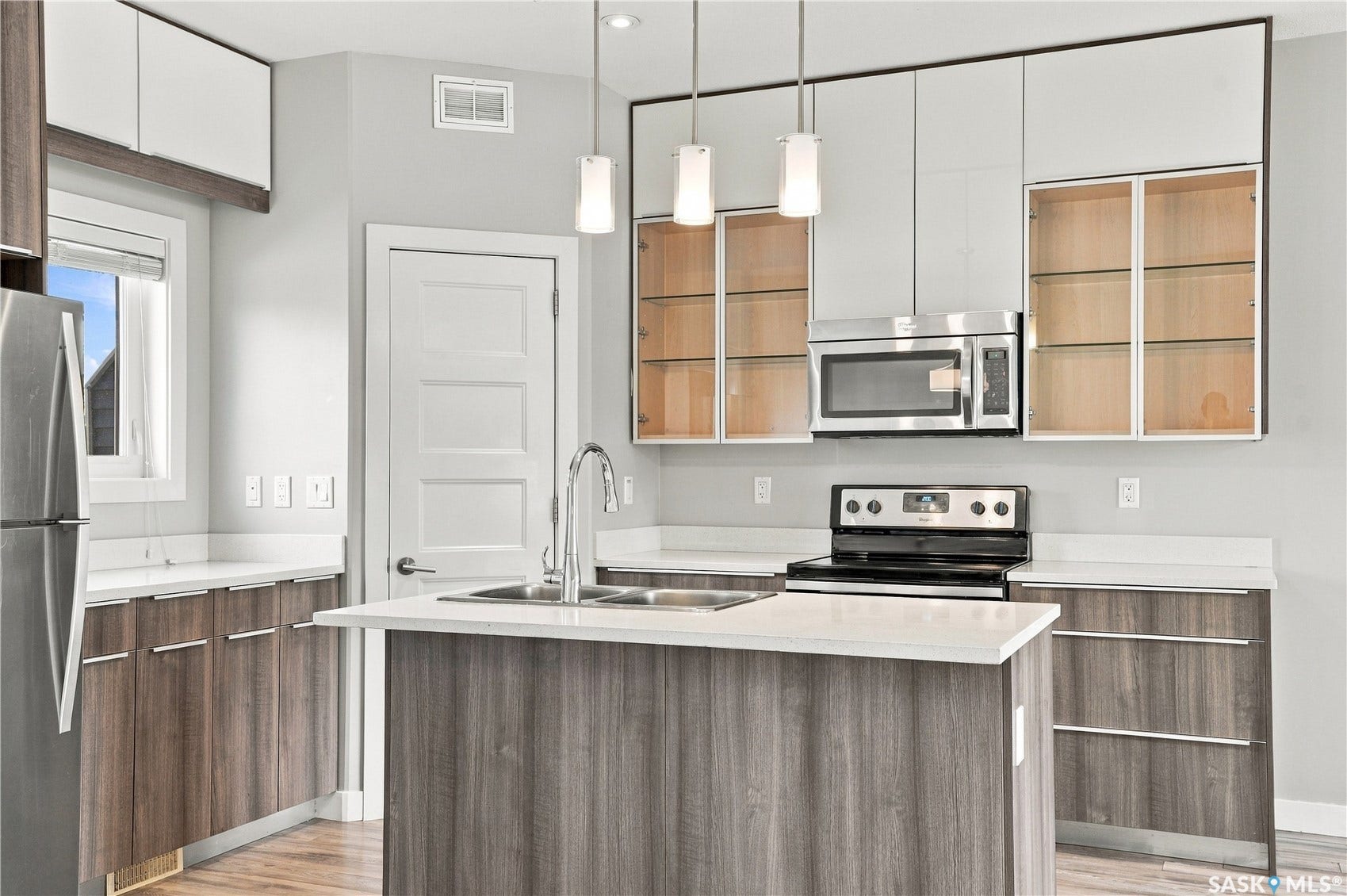 Modern kitchen featuring a two-tone cabinetry design with white upper cabinets and wood-finish lower cabinets, stainless steel appliances including a gas range and built-in microwave, white quartz countertops with a waterfall-edge island, pendant lighting, and brushed nickel faucet with pull-down spray