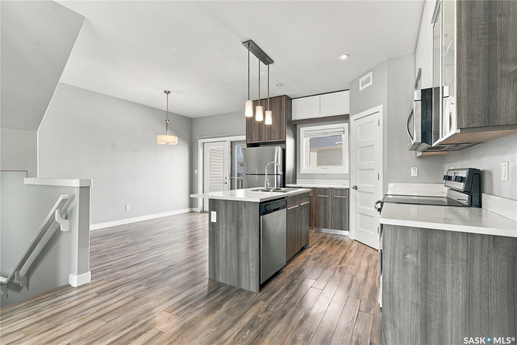Modern kitchen featuring stainless steel appliances, a center island with sink, pendant lighting, wood-finish flooring, and light-toned cabinetry