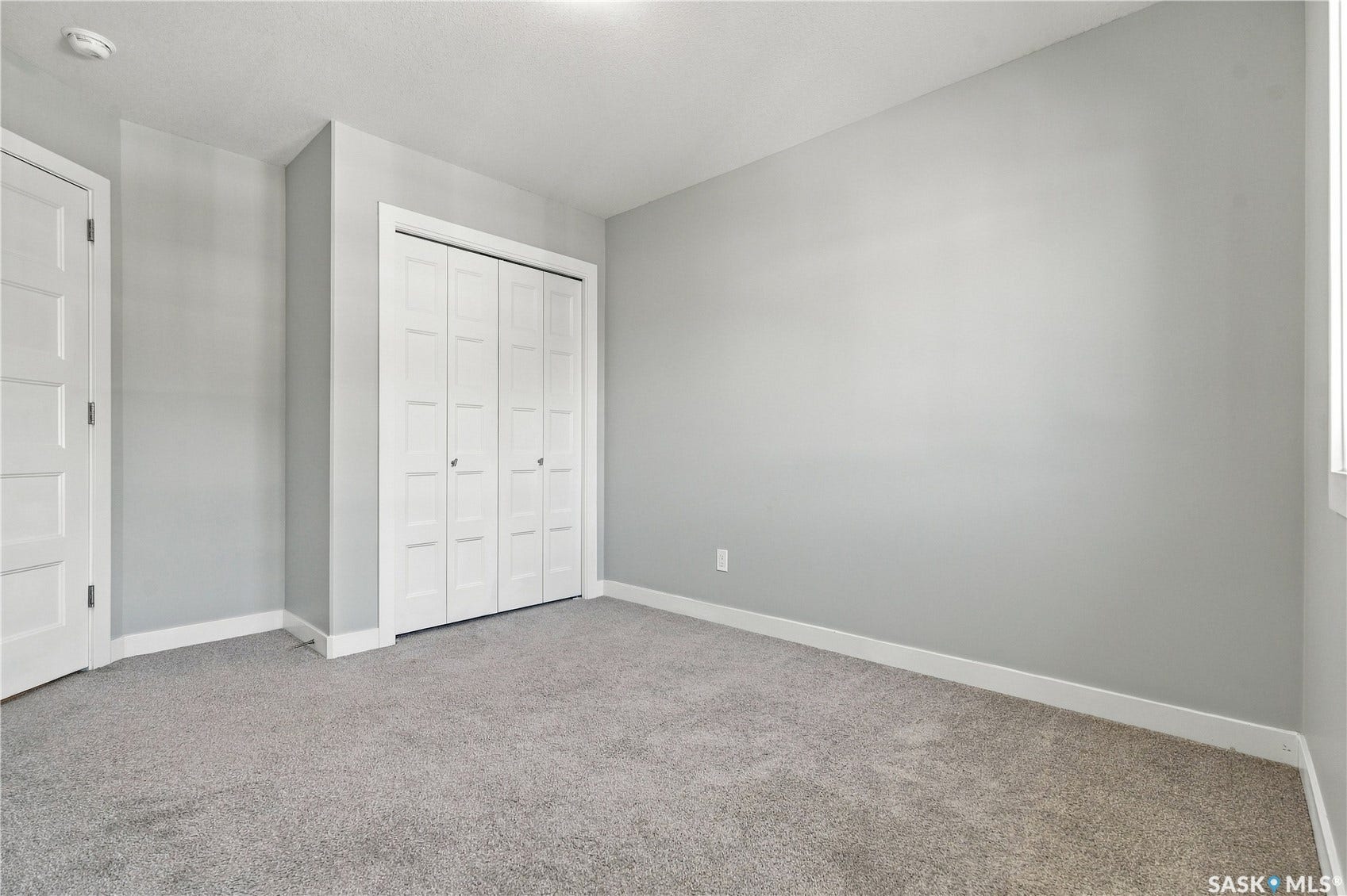 Spacious bedroom featuring neutral gray walls, carpeted flooring, a double closet with white panel doors, and recessed ceiling lighting
