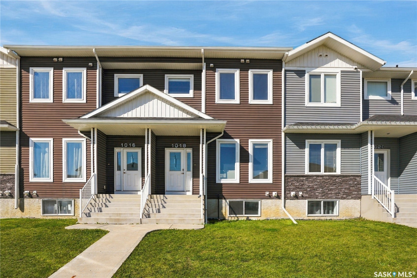 Townhome exterior featuring horizontal siding in brown and gray, white trim, multiple windows, covered entryways, and concrete walkways
