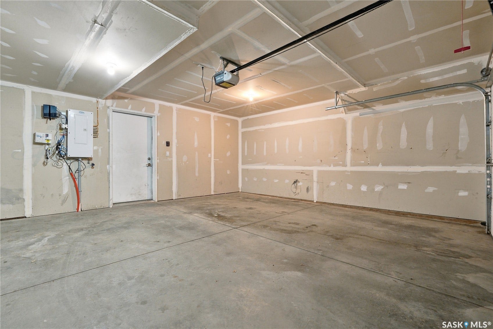 Concrete flooring, utility door, exposed drywall, overhead lighting, garage door opener