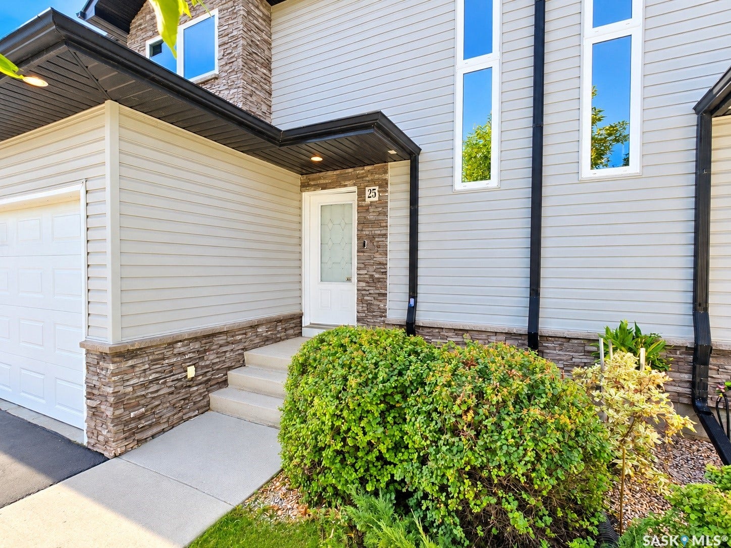 Light-toned siding exterior with stone accents, featuring a white paneled garage door and a white entry door with frosted glass detailing