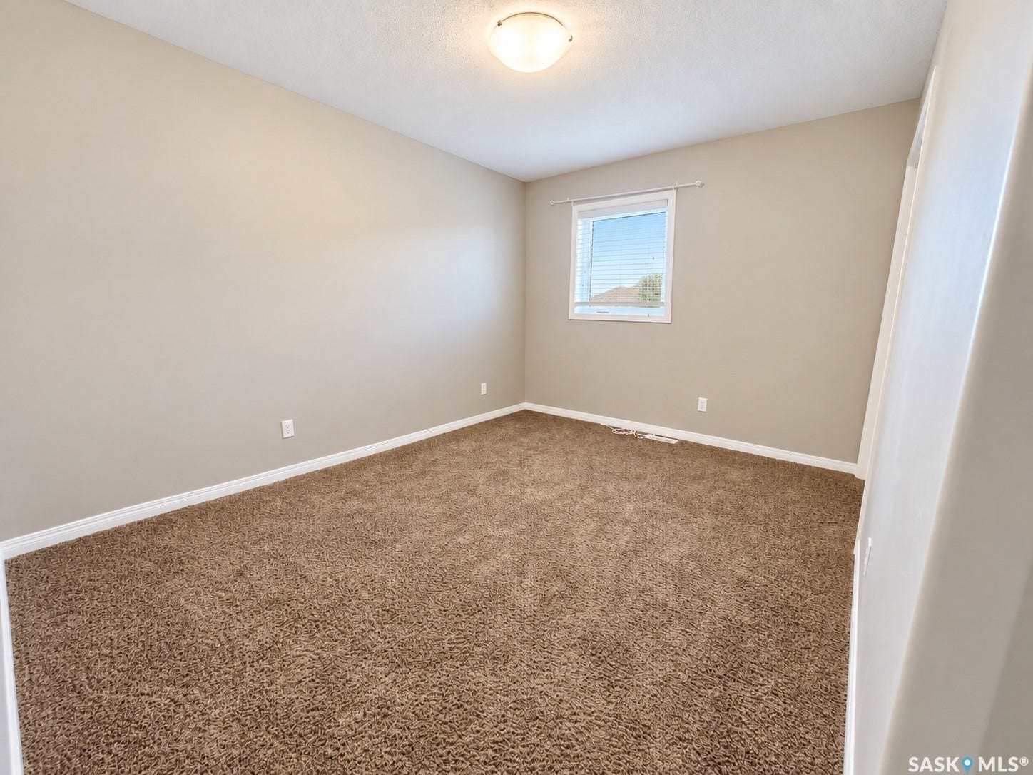 Neutral-toned walls, brown carpeting, and a white-framed window with blinds