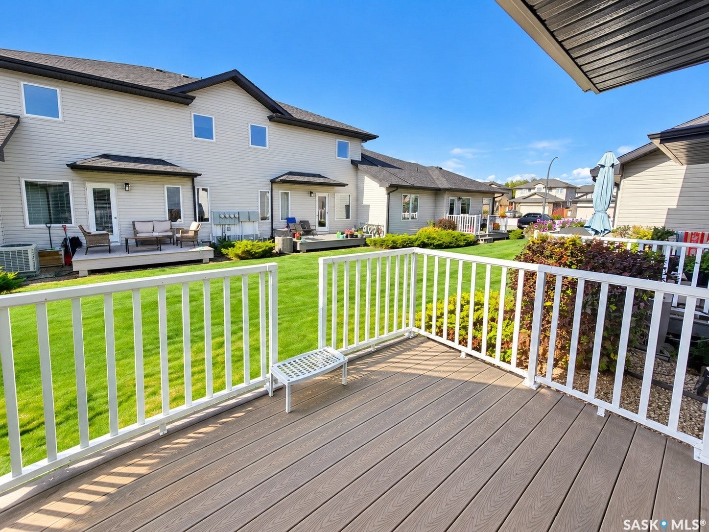 Expansive composite deck with white railings, offering views of a manicured lawn and mature landscaping