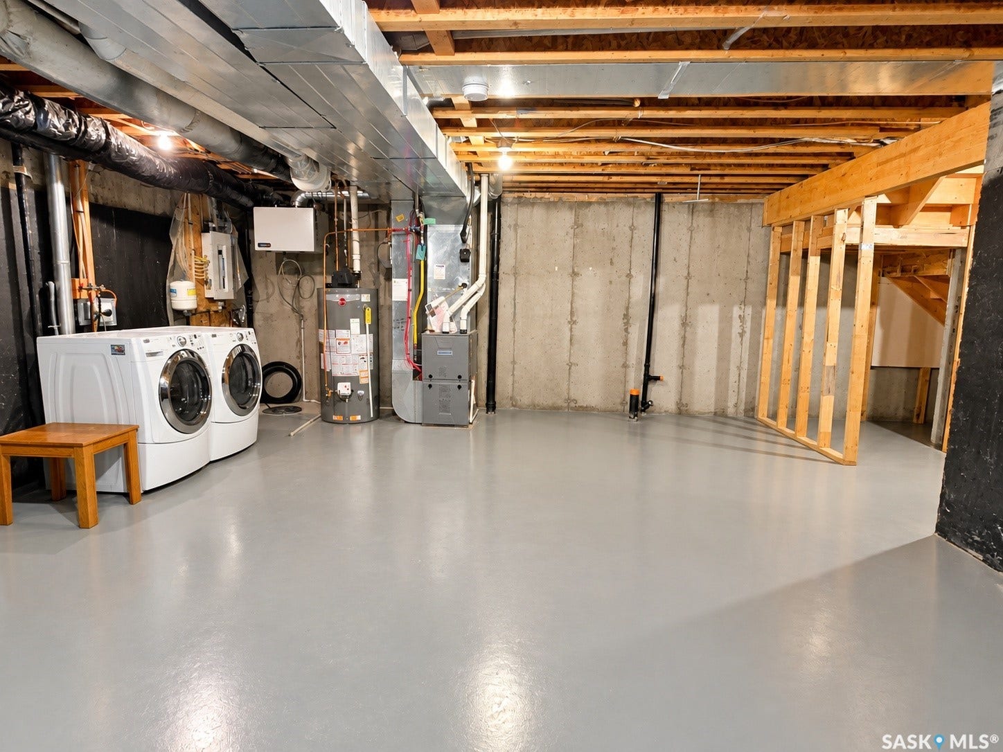 Spacious basement featuring painted concrete flooring, exposed ceiling joists, and concrete foundation walls