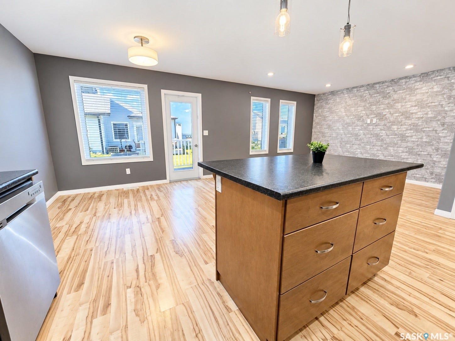 Wood-finish flooring throughout, central island with dark countertop, built-in dishwasher, recessed lighting, and an accent wall featuring stacked stone