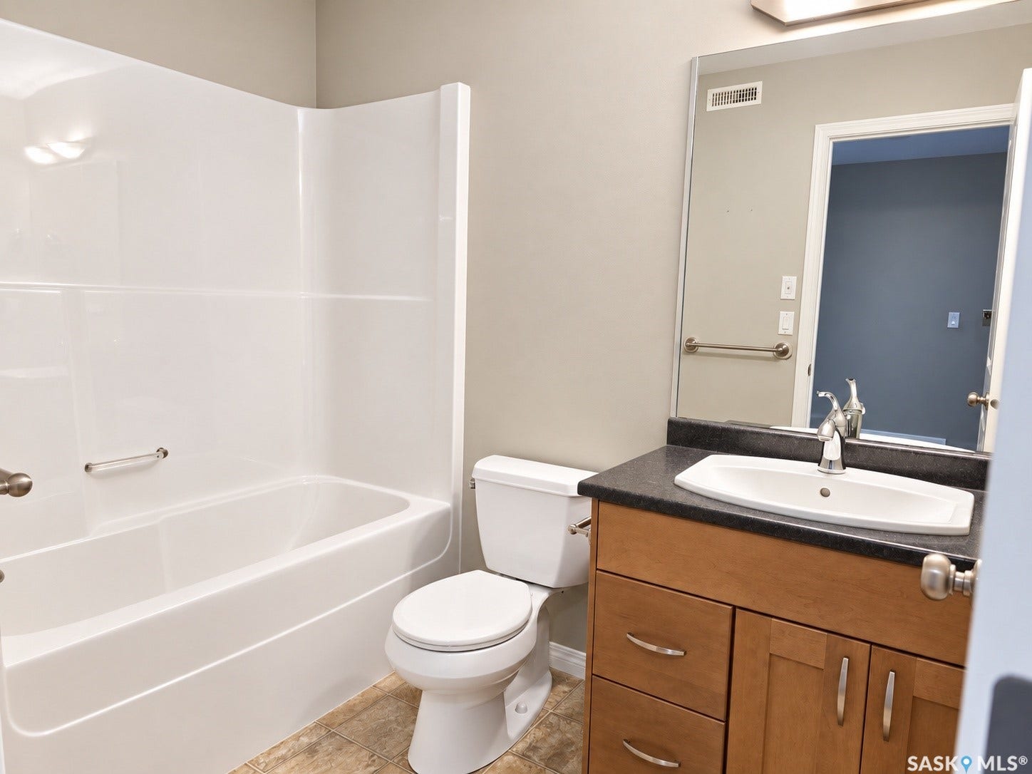 Bathroom featuring a white tub with integrated surround, wood-finish vanity with a dark countertop, and a white drop-in sink with a chrome faucet