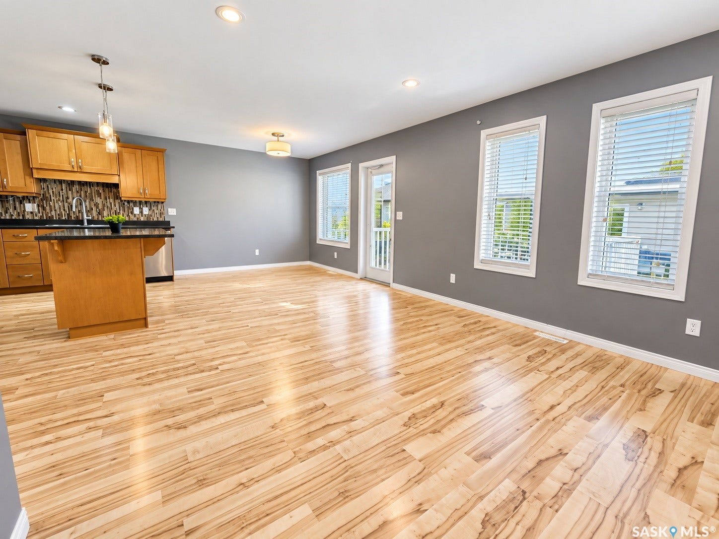 Open-concept living space with wood-finish flooring, recessed lighting, and a kitchen featuring wood cabinetry and a dark countertop island