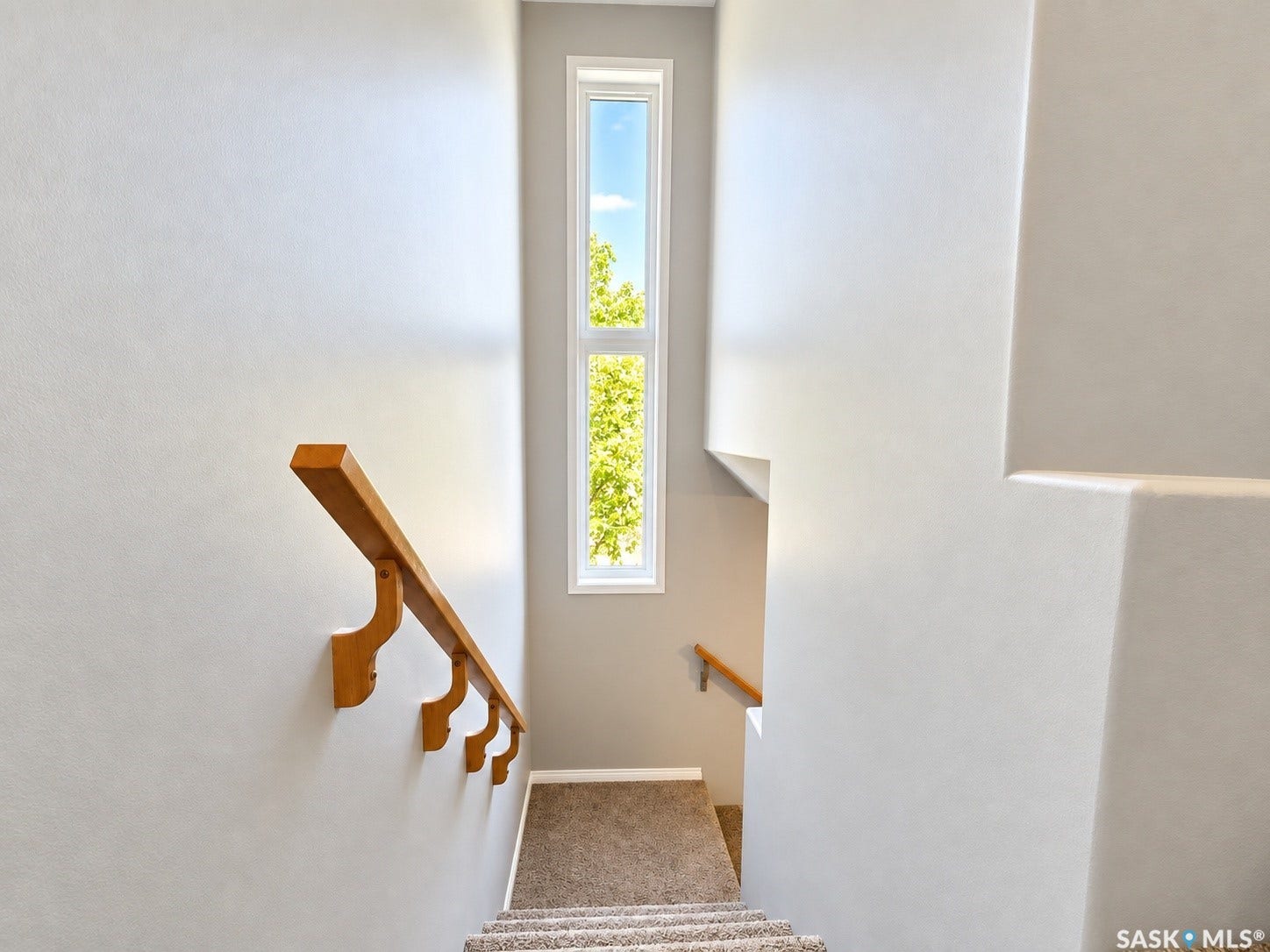 Stairwell with light gray walls, a tall vertical window, and wood handrails
